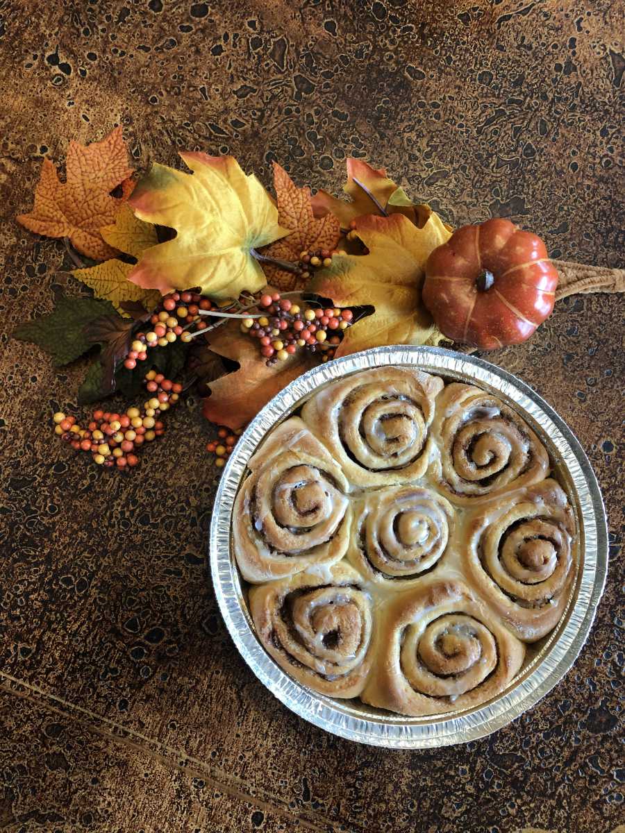 Tray of iced cinnamon rolls on a table with autumn leaves, berries, and a pumpkin for a cozy fall vibe.